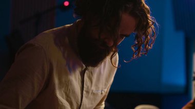 Müzisyen besteci profesyonel stüdyoda Midi kontrolör sentezleyicisi çalıyor, karıştırma konsolu üzerine müzik besteliyor. Kontrol odasında piyanonun elektronik klavyesinde performans sergileyen sanatçı. Kamera A.