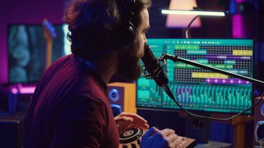 Yapımcı, şarkıları kaydetmek, montajlamak ve prodüksiyon sonrası ses seviyelerini ayarlamak için ev stüdyo mikrofonunda şarkı söylüyor. Ses mühendisi ses kayıtlarını düzenler, karıştırma konsolu. Kamera A.