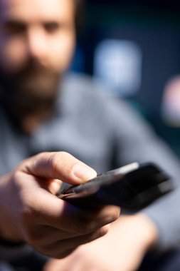 Bulanık arkaplanlı bir adam tarafından kullanılan uzaktan kumandaya odaklanın. Yayın hizmetleri üzerine bir film seçmek için, dinlendirici bir akşam geçirmek için. TV 'de daire değiştiren kanallarda görüntüleyici, görüntüyü kapat