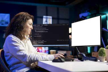Evdeki izole ekran bilgisayarında yazılım hata ayıklaması yapan programcı, monitörlerde gösterilen bozuk kod satırlarını kontrol ediyor. Oturma odasındaki kadın model bilgisayardaki kodlama sorunlarını düzeltiyor