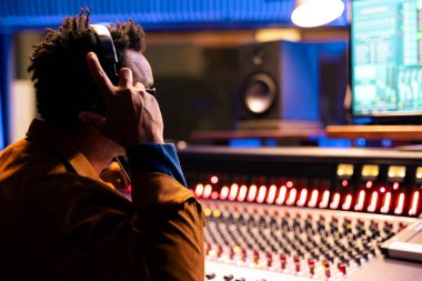 Müzik yapımcısı şarkıları düzenlerken ve işlerken kulaklık kullanıyor, profesyonel stüdyodaki kontrol odasında kayıt yapıyor. Ses mühendisi, prodüksiyona ses efekti eklemek için düğmelere basıyor.