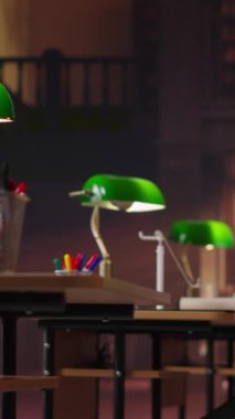 Büyük kitaplıkların ve çalışma alanlarının yer aldığı dikey video geleneksel kütüphanesi, eski bir estetik için ahşap masalara yerleştirilmiş yeşil lambalar. Bilimsel eğitimin eski moda cazibesi.