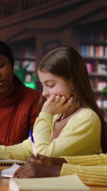 Kütüphanede çeşitli öğrencilere danışmanlık yapan, müfredat kitaplarıyla dolu bir akademik kütüphanede öğrenen dikey video Amerikalı profesör. Kadın öğrencilerine edebiyat dersi veriyor.