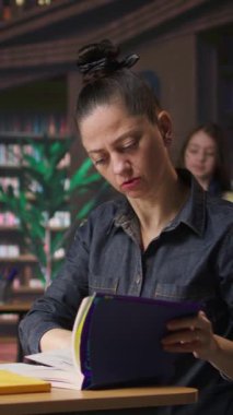 Bir halk kütüphanesinde akademik kaynaklara ve başarı için rehberliğe odaklanmış, yeni notlar üzerinde çalışan Dikey Video Profesyoneli yazar ve kütüphaneci. Eğitici bilgi toplayan bir kadın. Kamera A.