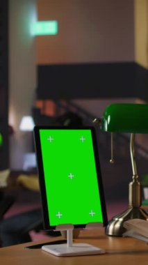 Dikey Video Öğrencisi kız kütüphane masasındaki tablette kitaplığın yanında bir kitap okuyarak akademik veritabanını araştırma için kullanıyor. Okul ödevlerini tamamlamak ve eğitim becerilerini geliştirmek.