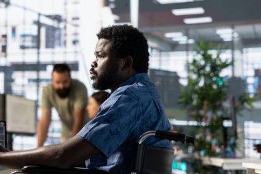 Belden aşağısı felçli biri ofiste, tekerlekli sandalyede oturuyor ve takım projesi için araştırma yapıyor. Özürlü bir adam kapsayıcı işyerindeki bilgisayar ekranına bakıyor, görevleri çözüyor