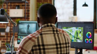 Erkek video üreticisi, zaman çizgisi düzenleme ve video üretimini yönetmek için profesyonel teknoloji araçları ve kurgu yazılımları kullanarak modern bir ofiste bir multimedya projesini düzenler. Evden çalışıyorum. Kamera B.