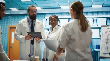 Doktor ve hemşireler hastane ortamında en iyi tedaviyi sunmayı hedefleyen sağlık raporlarını ve test sonuçlarını gözden geçiriyorlar. Muhtelif sağlık görevlileri kontrol için sağlık kayıtlarına bakıyorlar. Kamera B.