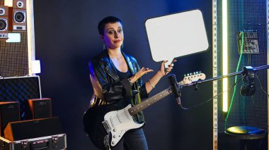 Dişi rock yıldızı, boş karton konuşma baloncuğunu gösteriyor. Bir sanatçı olarak isyankar, grunge tavrını sergiliyor. Kadın müzisyen reklam panosuyla reklam yapıyor. Kamera A.