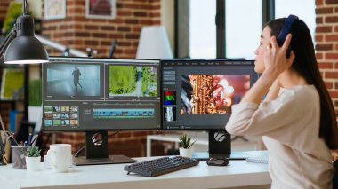 Asyalı film yapımcısı kadın kulaklık takıyor ve video yapımında çalışıyor, video klipleri karıştırıyor. Prodüksiyon sonrası renk değerlendirmesi için mükemmel bir yazılımla ofis kurulumu. Kamera B.