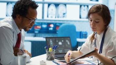 Tıbbi uzman test sonuçlarını sağlık ortamındaki bir hastayla tartışıyor, doğru tıbbi analiz ve danışma için teşhis araçları ve bilgisayar teknolojisinden faydalanıyor. Kamera A.