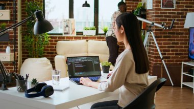 Asyalı serbest çalışan kadın evdeki modern bir ofiste bilgisayar bilimi için dizüstü bilgisayarını kullanarak programlama kodu üzerinde çalışıyor. IT uzmanı kodlamayı, web geliştirmeyi ve dijital yeniliği destekliyor. Kamera A.