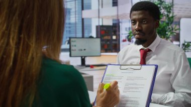 İK personeli ve başvuru sahibi, mülakat sırasında iş sözleşmesi şartlarını tartışıyor, açıklamalar ve açıklamalar sunuyor. Üst düzey bir ofiste iş sözleşmesini okuyan iş adayı. Kamera B.