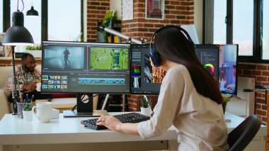 Asyalı film yapımcısı kadın kulaklık takıyor ve video yapımında çalışıyor, video klipleri karıştırıyor. Prodüksiyon sonrası renk değerlendirmesi için mükemmel bir yazılımla ofis kurulumu. Kamera A.