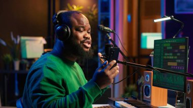 Erkek besteci, kendi yarattığı bir şarkıyı söyleyerek sesini mikrofona kaydediyor. Karıştırma ve ustalaşma tekniklerini uygulamak için ses dosyaları ve şarkı sözleri kullanan yetenekli bir sanatçı. Kamera A.