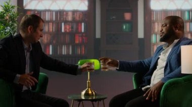 Sosyetenin üst düzey seçkin üyeleri kadeh kaldırmak için viski bardaklarını tokuşturuyorlar. Ailelerinin servetini ikiye katlamak için yeni ortaklıklarını kutluyorlar. Sosyal kulüpteki yaşlı paralı beyler. Kamera A.