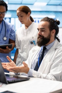 Bir araştırma toplantısında uzman doktorlara danışmanlık yapan, bir hastane konferans odasında işbirliği yapan profesyonel bir doktor. Sağlık görevlileri hasta geçmişlerini gözden geçiriyor ve uygun tedavi seçenekleri planlıyorlar.