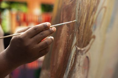 Afrikalı Amerikalı sanatçı boya fırçasıyla tuvale akrilik boya uyguluyor, sanat galerisi için bir başyapıt yaratma yeteneğini gösteriyor. Profesyonel malzemelerle çalışıyor. Kapat..