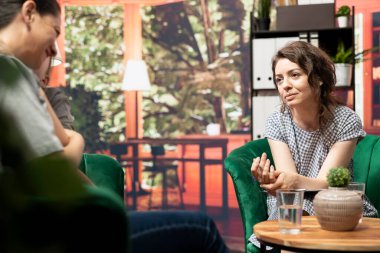 Annesiyle oturan genç kız, endişe ve duygusal sorunlar için terapi arıyor. Psikolog ruh sağlığı ve hormonal değişimlerle ilgili rehberlik sunuyor. Aile terapisi.