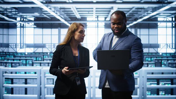 African american admin greeting inspector arriving in data center to supervise operations. IT expert in server hub workspace doing hand shake with supervisor monitoring performance, camera B