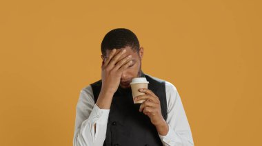 Tired overworked waiter drinking a coffee cup to relax after long shift, working in catering and service oriented environment. Employee feels fatigued and serving caffeine drink. Camera A. clipart