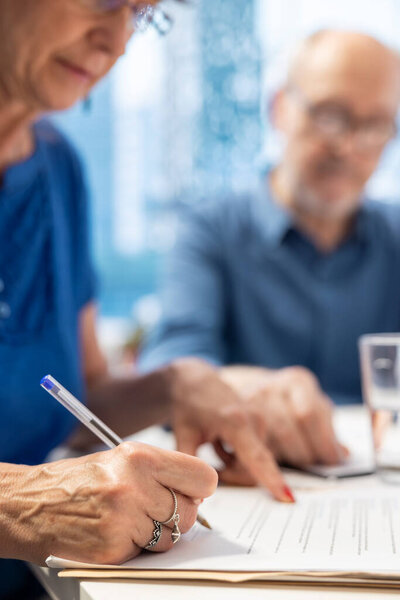 Mature person signing the financial contract in modern office, agreeing to retirement and pension plan to secure life savings. Senior woman signs the document terms for income. Close up.