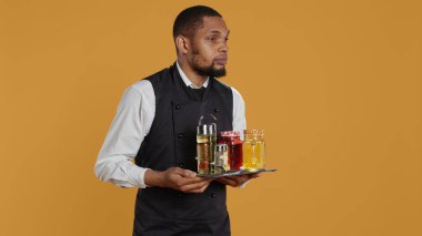 Waiter bringing drinks in glasses on a tray for clients at a table, serving lemonade to customers before their dinner. Professional staff serving people at a five star restaurant. Camera B. clipart