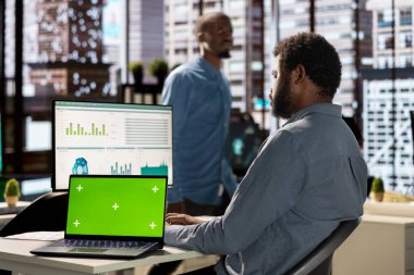 Siyahi işadamı finansal verileri krom ekranın yanında analiz ediyor, şirket stratejilerini bilgisayarda gözden geçiriyor ve iş geliştirme ve karar verme sürecine katkıda bulunuyor. Başarılı öngörü.