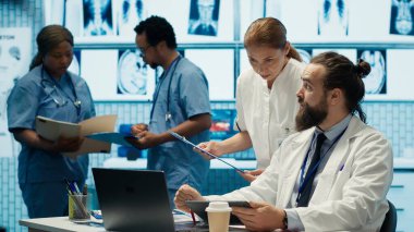 Bir tedavi merkezinde bulunan sağlık uzmanları, X ışını taramalarını ve test sonuçlarını analiz ederek, hastalıkların önlenmesi için teşhis ve tedavi planları üzerinde işbirliği yapıyorlar. Toplu iş. Kamera A.