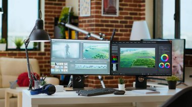 Oturma odasındaki modern dijital çalışma alanı teknoloji ve verimliliğe odaklandı, video oluşturma için post prodüksiyon araçlarını gösteren çift monitörler. Temiz masa kurulumu verimli video üretimini destekliyor.