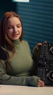 Dikey videolu neşeli kız DJ pikapları karıştırıyor, çevrimiçi yayın kanalı için müzik prodüksiyonu dersi veriyor. Gülümseyen genç içerik yaratıcısı stereo ses karıştırıcı, kamera A ile oynuyor.