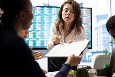 Finansal uzman, bir konferans odasında kağıtlarla ilgili istatistik verileri gösteriyor, personelle aylık sunum için brifing veriyor. Pazar ihtiyaçlarına uyum sağlamak için satış raporlarını inceleyen iş arkadaşları.