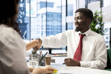 Cheerful HR professional shaking hands with person after identifying right candidate for job opening. Upbeat manager shaking hands with man after finishing screening process clipart