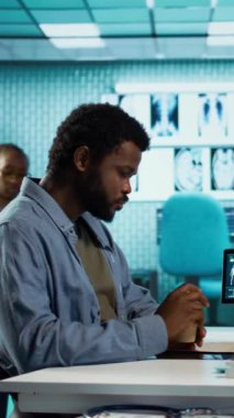 Dikey video uzmanı, kabinede termometresi olan genç bir hastaya danışarak, kontrol ziyareti sırasında modern aletlerle humma ölçümü yapıyor. Doktorla profesyonel etkileşim. Kamera B.