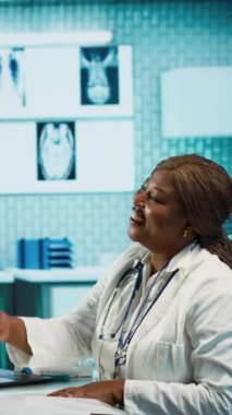 Dikey video, Afrikalı Amerikalı kadın doktor rutin check-up ziyareti sırasında bir kıza radyoloji sonuçlarını açıklıyor. Teşhis ve tedavi tavsiyelerine odaklanıyor. Özel bir ortamda etkili iletişim