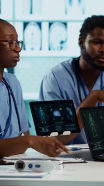 Dikey video Afrikalı Amerikalı pratisyen hekimler kabinede bir sağlık ekibini yönetiyor, MRI görüntüleme sonuçlarını analiz ediyor ve doğru teşhis ve etkili tedavi sağlıyor. Tıbbi tesis