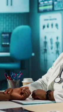 Dikey video, Afrikalı Amerikalı doktor nabız ve kalp atışı kontrol sırasında kol saatindeki fitness takip cihazına bakan bir hasta için. Kalp atış hızı ölçümü