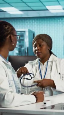 Dikey video Afrikalı Amerikalı kadın doktor steteskopla solunum danışmanlığı yapıyor, kalp atışlarını ve akciğerlerin normal çalışmasını dinliyor. Doktor nabzını kontrol ediyor.