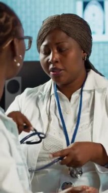 Dikey video Afrikalı Amerikalı kadın doktor steteskopla solunum danışmanlığı yapıyor, kalp atışlarını ve akciğerlerin normal çalışmasını dinliyor. Doktor nabzını kontrol ediyor.