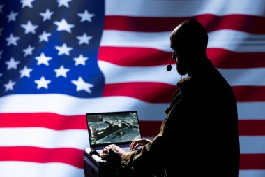 ABD askeri subayı saklanan düşmanların yerini tespit etmek için laptop 'da hedef alma yazılımı kullanıyor. ABD bayrağı üzerinde izole edilmiş bir asker, uyduyla ülkeyi tehdit eden teröristleri tespit ediyor.