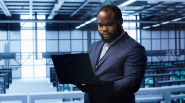 Afrikalı Amerikalı bilişim operatörü veri merkezi ekipman ömrünü uzatmak için dizüstü bilgisayar kullanıyor. Bilgi işlem uzmanı sunucu merkezinde çalışma alanı izleme sunucu ana bilgisayarlarında dizüstü bilgisayar, kamera A 'yı kullanarak