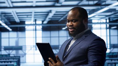 Sunucu odasındaki programcı aktarım oranlarını etkileyen ağ sorunlarını düzeltmek için tablet kullanıyor. Veri merkezindeki Afrikalı Amerikalı adam ana bilgisayarları etkileyen hataları düzeltiyor, kamera A