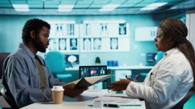 Siyahi erkek hasta, tarama için sıhhiyeye röntgen testi sonuçlarını getiriyor. Teşhis raporlarını inceliyor. Tıbbi uzman kabinedeki radyografi filmini değerlendiriyor. Kamera B.