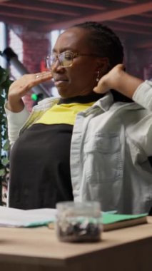 Uzun süre masa başında oturduktan sonra apartmanda eklemlerini geren dikey video kumandalı bir çalışan. Ofisteki kadın, yanlış poziyondan dolayı acı çektikten sonra kas egzersizi yapıyor.