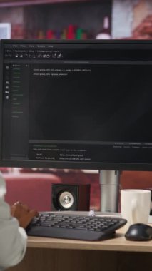 Ana ofisteki dikey video bilişim teknisyeni bilgisayar ekranında UI 'ye bakıyor, programlama metnini çalıştırıyor. Modern apartman ve kamera kodlarını yazmak ve test etmek için kodlama uygulaması kullanan uzaktan çalışan