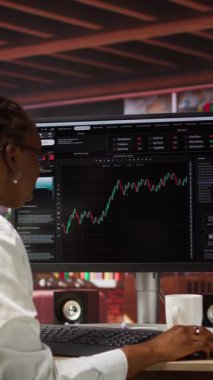 Hisse senedi alıp satmak için bilgisayar kullanan, dosya okuyan, piyasa eğilimleri ve dalgalanmalardan faydalanmayı amaçlayan dikey video günü tüccarı. Yatırımcı bilgisayar monitöründe hisse senedi önyükleme eğilimleri, kamera