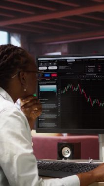 Hisse senedi almak ve satmak için bilgisayar kullanan dikey video günü işlemcisi, karları maksimuma çıkarmak için doküman dosyalarını karıştırıyor. Bilgisayar ekranındaki borsa grafiklerine bakan yatırımcı