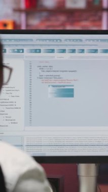 Ana ofisteki dikey video kadın bilgisayar ekranında UI 'ye bakıyor, programlama kodunu yazıyor ve çalıştırıyor. Kullanılan kodlama uygulaması UI yazılım ve test kodu modern apartman, kamera B