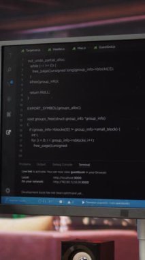 Yazılım yaratmak ve algoritmaları uygulamak için kullanılan kodlama uygulamalı dikey video masası. Rahat, parlak oturma odasında uygulamalar oluşturmak için kullanılan bilgisayar ekranındaki kod düzenleyicisi