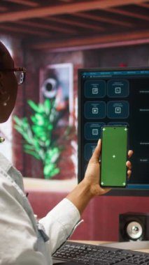Ana ofisteki bilgisayar ekranında izole ekran akıllı telefonu ve AI LLM sohbet robotu kullanan dikey video kadın. Krom anahtar telefonu olan kişi monitörde yapay zeka sohbet robotu kullanıyor. Kamera A.